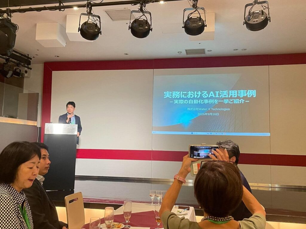 Yuji Nakayama at the podium in front of his title slide on AI in practice