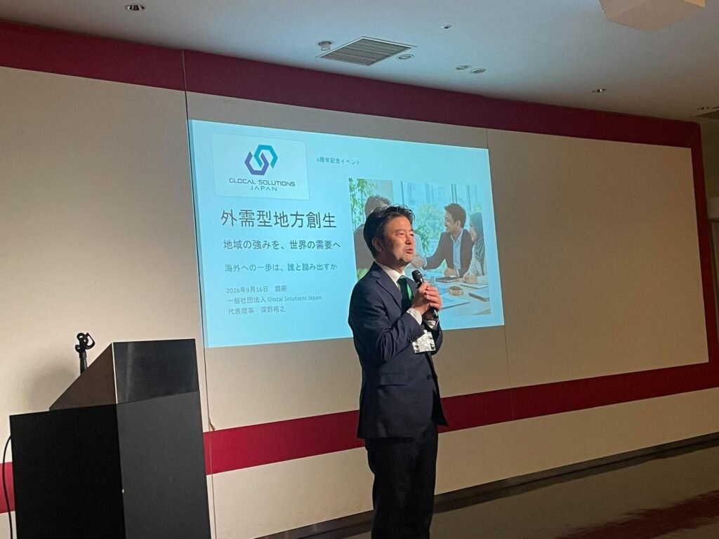 Representative Director Hiroyuki Fukano speaking in front of his title slide on regional revitalization driven by overseas demand